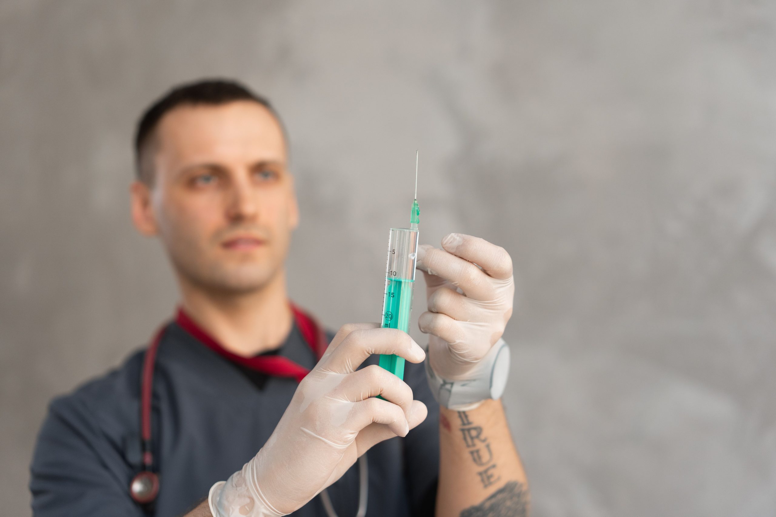 Medical practitioner in gloves holding a syringe ready for injection.